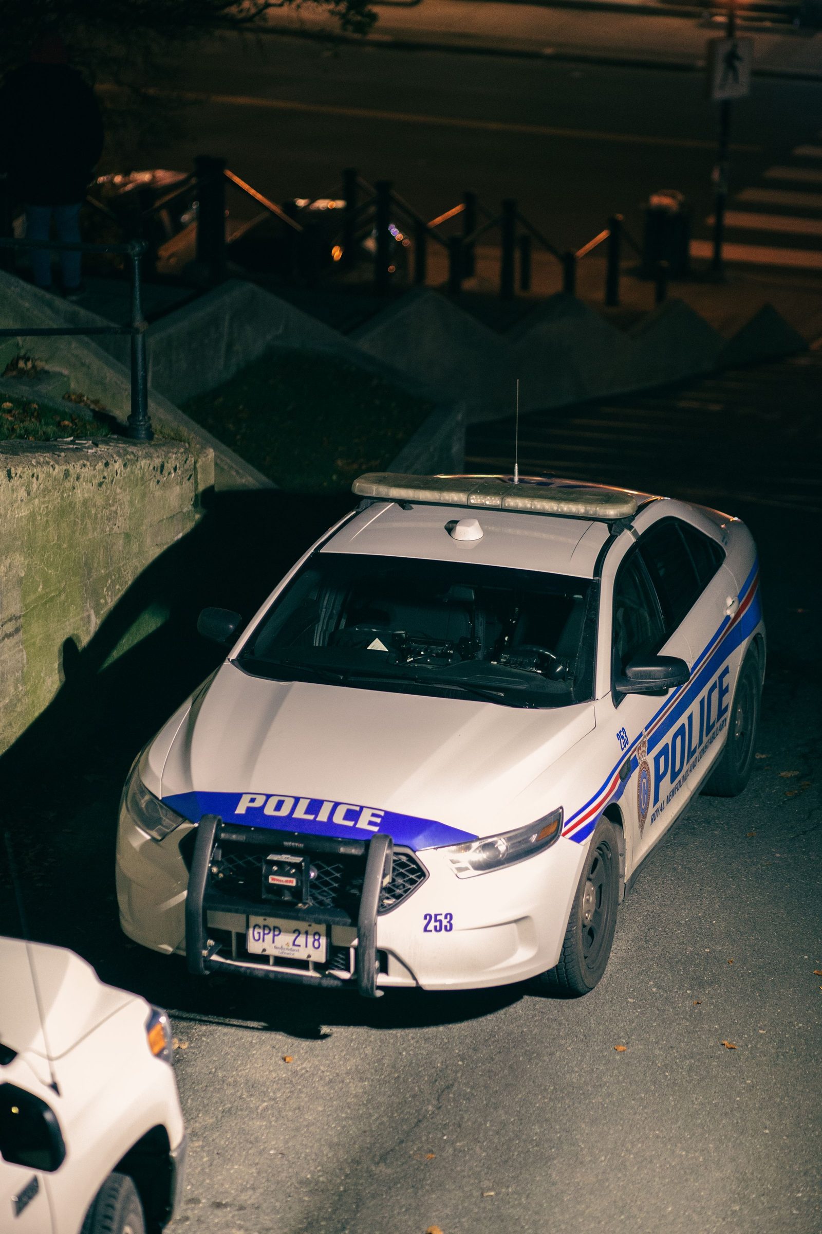A patrol car parked on a street at night beside a flight of steps